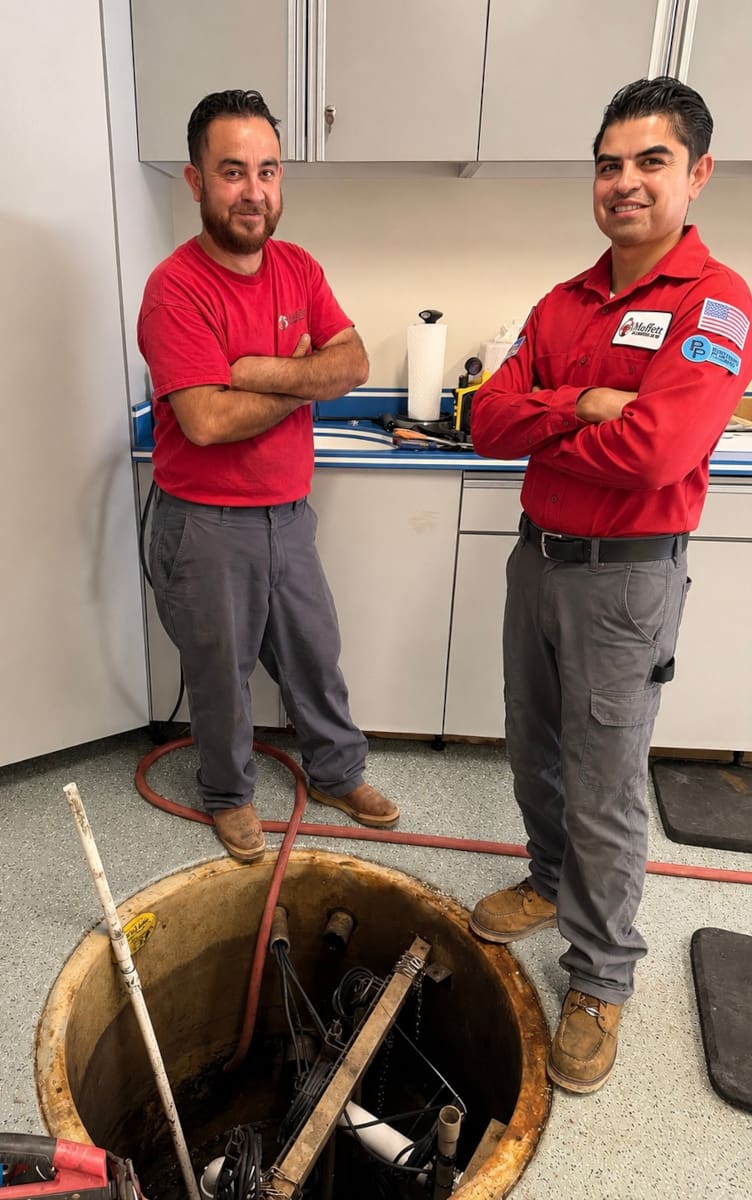Moffett Plumbing & Air technicians standing beside an open sump pump pit during a sump pump inspection and maintenance service.